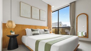 Quarto de hotel moderno com uma cama grande, cabeceira de madeira, uma mesinha de cabeceira com uma planta e uma janela ampla com vista para edifícios.