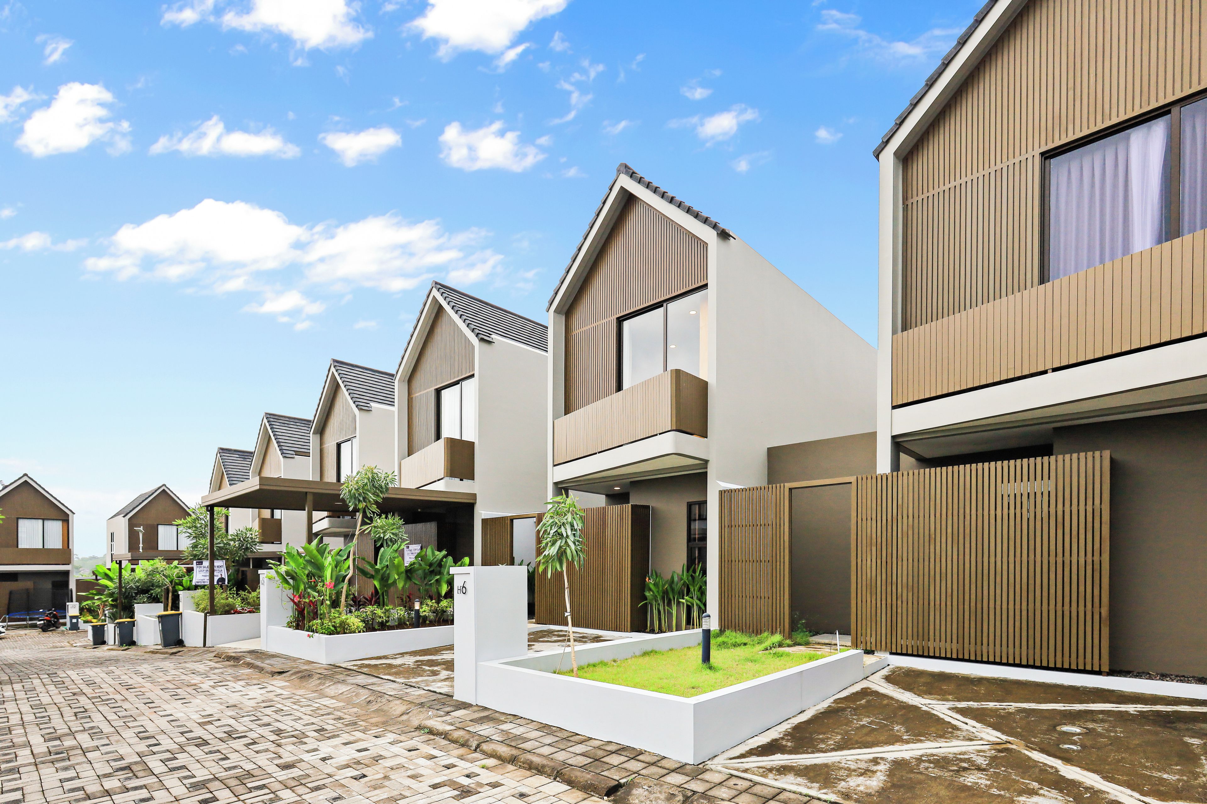 A modern residential building with a flat roof, large windows, and a paved courtyard with greenery.