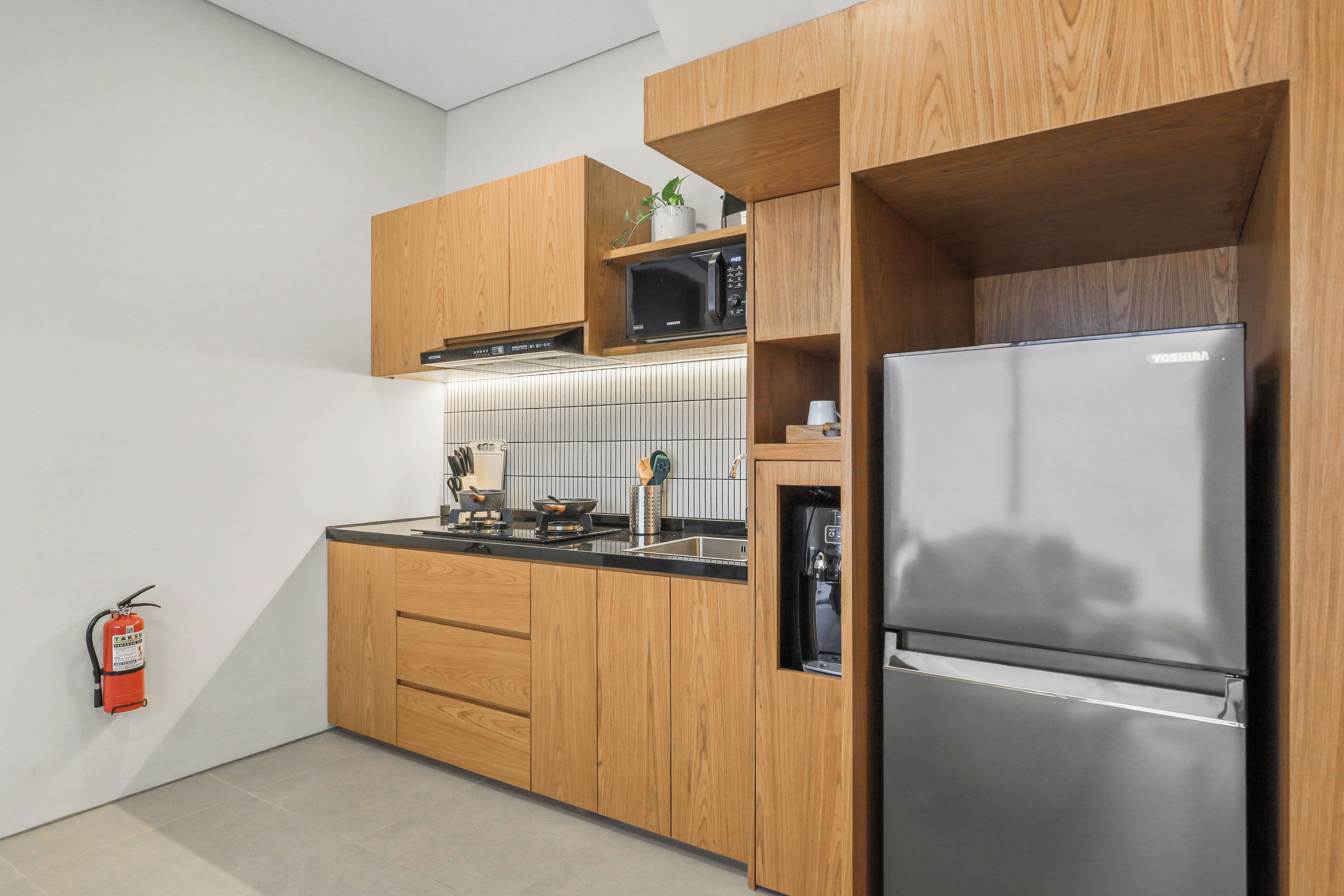 Eine moderne Küche mit Holzschränken, einem Edelstahlkühlschrank, einer Mikrowelle und einem eingebauten Herd.
