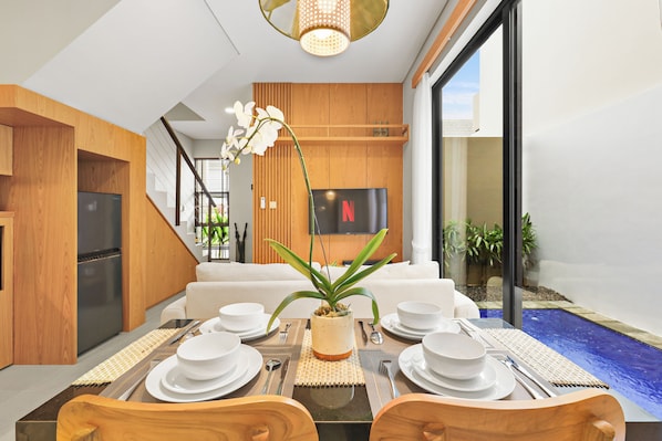 A modern dining area with a table set for four, a television mounted on the wall, and a view of the outside.