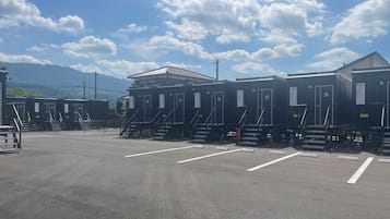 A row of portable cabins with numbered doors, a parking lot, and a mountain in the background.