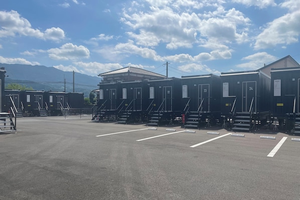 A row of portable cabins with numbered doors, a parking lot, and a mountain in the background.