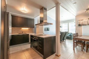 Una cocina moderna con armarios oscuros, una isla central y una zona de comedor con mesa y sillas de madera.