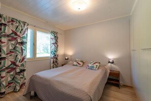 Un dormitorio con una cama, dos lámparas de noche, una ventana con cortinas y piso de madera.
