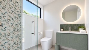 Ein modernes Badezimmer mit Duschkabine aus Glas, Toilette, Waschbecken mit grüner Rückwand und rundem Spiegel.