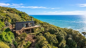 Una proprietà costiera con terrazza in legno, una scala che conduce a un balcone e vista sull'oceano.