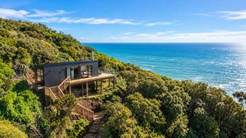 A coastal property with a wooden deck, a staircase leading to a balcony, and a view of the ocean.