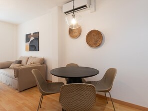 A modern living room with a round dining table, wicker chairs, a sofa, and a wall-mounted air conditioner. - Central two-bedroom apartment (Málaga)