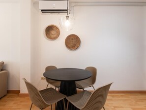 A dining area with a round table and four wicker chairs, a wall-mounted air conditioner, and two woven wall decorations. - Central two-bedroom apartment (Málaga)