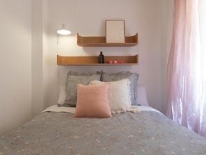 A bedroom with a bed, pillows, a nightstand, a lamp, and a shelf with a book and a bottle. - Central two-bedroom apartment (Málaga)