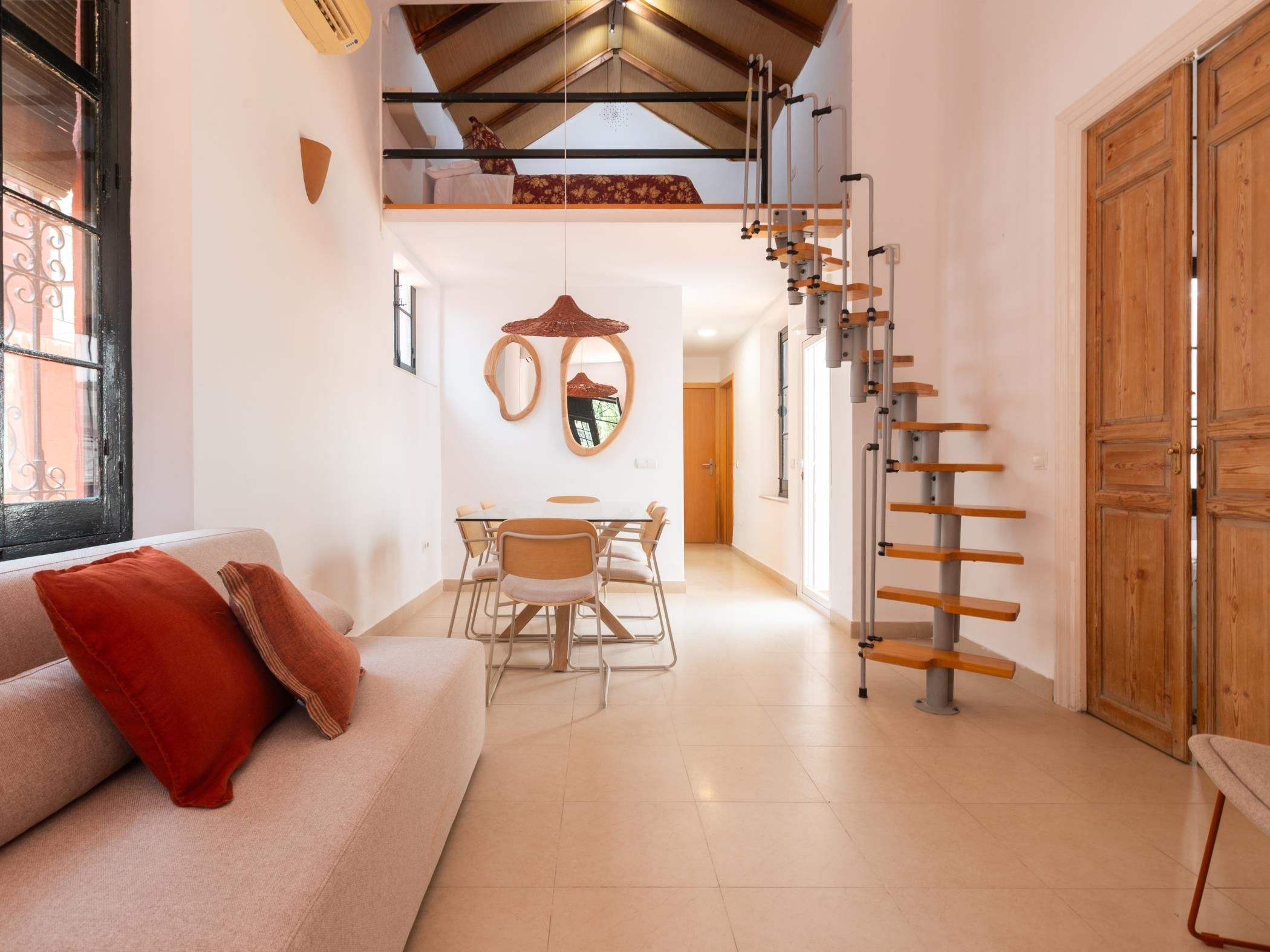 Ein modernes Interieur mit einer Couch, einem Esstisch, Stühlen, einer Treppe und einer großen Holztür.