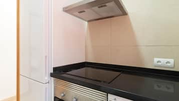 Una cocina con un refrigerador blanco, una estufa negra y un salpicadero de azulejos color beige.