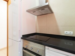 Una cocina con un refrigerador blanco, una estufa negra y un salpicadero de azulejos color beige.