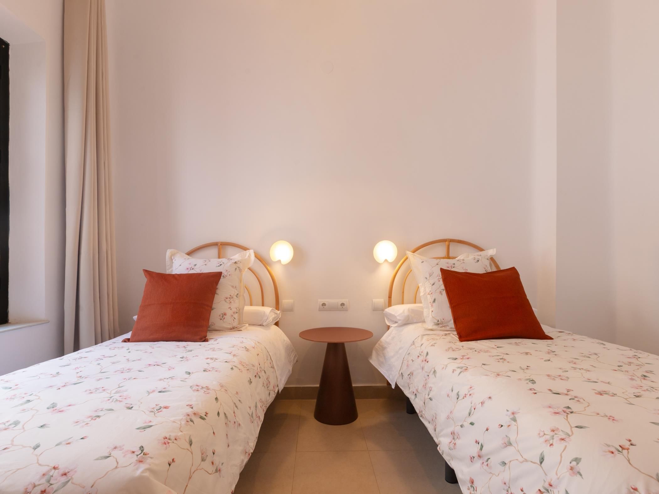 Habitación con dos camas, cada una con cabecero, una mesita redonda y un enchufe en la pared.