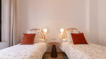 Habitación con dos camas, cada una con cabecero, una mesita redonda y un enchufe en la pared.