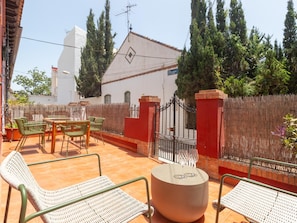 Une terrasse extérieure avec une table et des chaises, un mur rouge et un portail.
