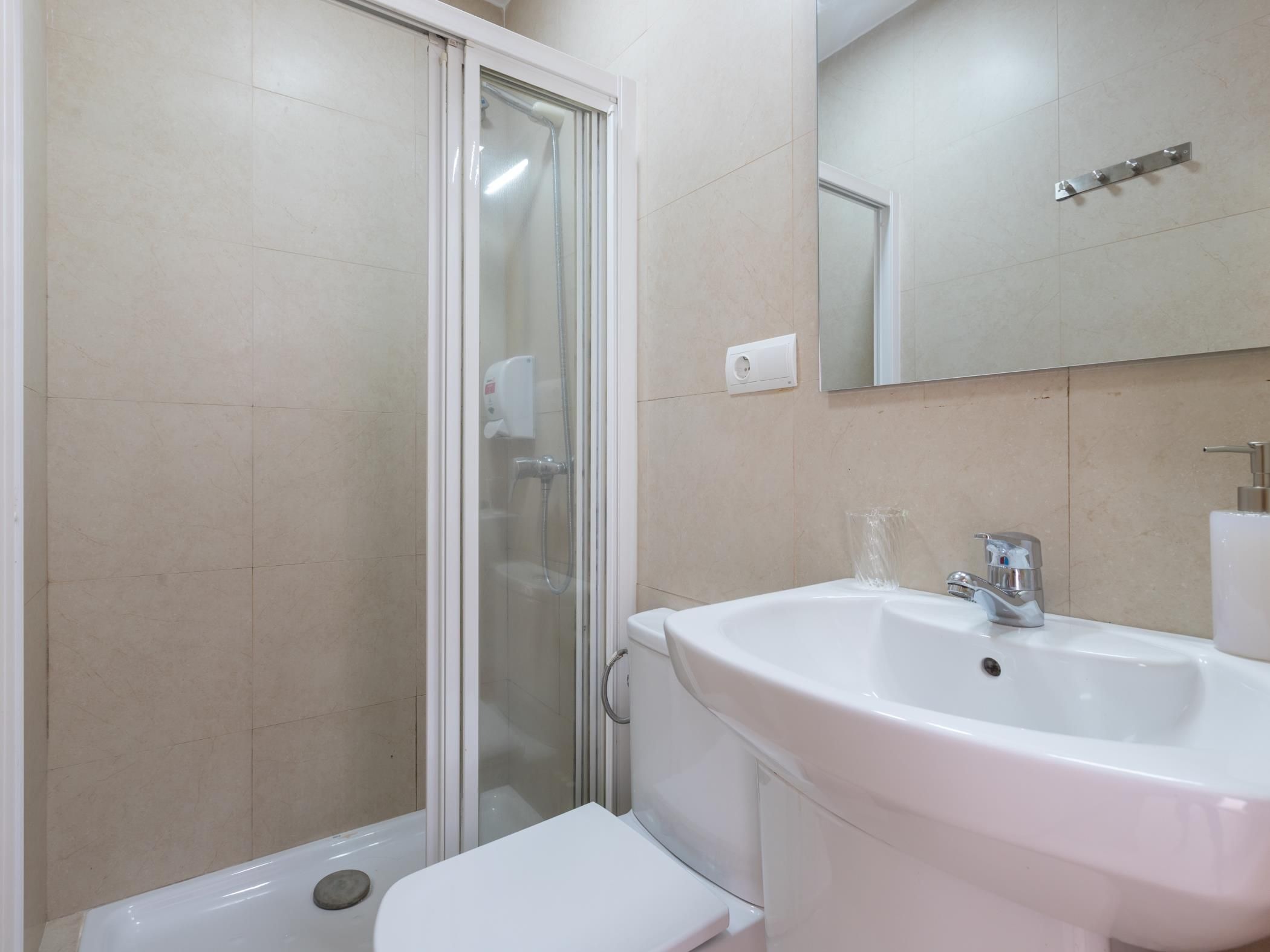 Un baño con cabina de ducha de vidrio, un lavabo blanco y un espejo sobre el lavabo.