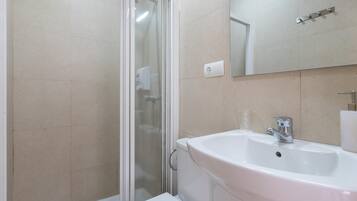 Un baño con cabina de ducha de vidrio, un lavabo blanco y un espejo sobre el lavabo.