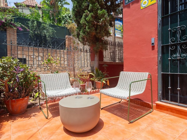 Une terrasse extérieure avec deux chaises en osier blanc, une table ronde et un pot de fleurs.