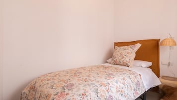 Una cama individual con una colcha estampada, cabecera de madera, lámpara de noche y un cojín marrón.