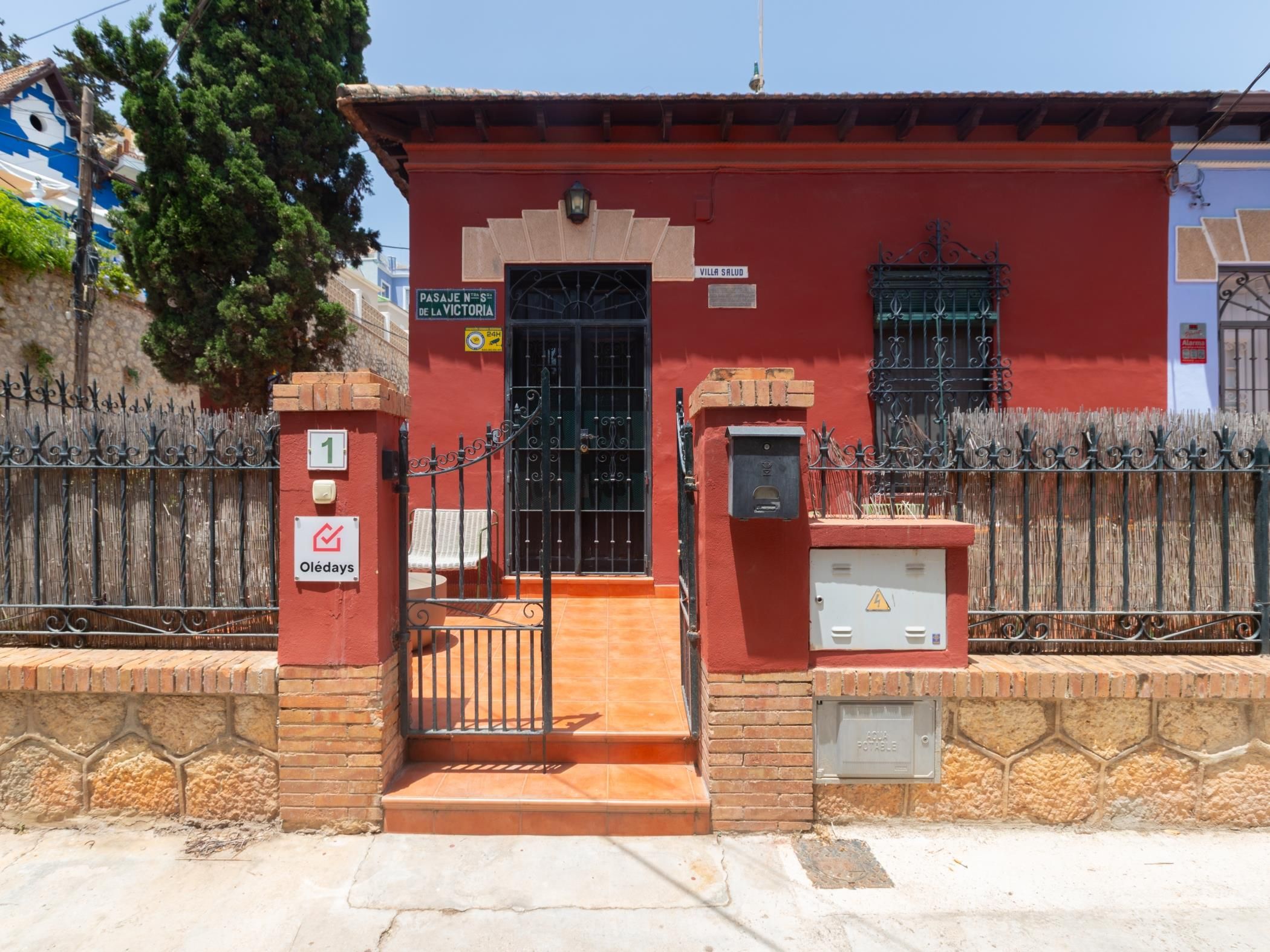 Un edificio rojo con entrada protegida por una reja, un cartel que indica 'Villa Salud' y un letrero que anuncia servicio las 24 horas.