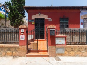 A red building with a gated entrance, a sign indicating 'Villa Salud,' and a 24-hour service sign.