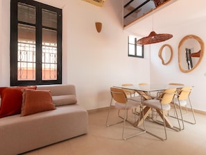 A modern living room with a sofa, a dining table with chairs, and a large window with decorative iron bars.