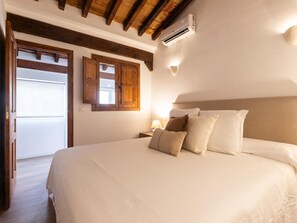 Ein Schlafzimmer mit einem großen Bett, Holzbalken an der Decke, einer Klimaanlage und einem Fenster mit Holzläden.