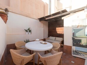 Eine Terrasse mit rundem Tisch, Korbstühlen, einer Sitzecke und Topfpflanzen.