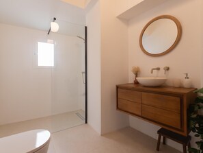 Ein Badezimmer mit einem Holzbadschrank, einem runden Spiegel, einem weißen Waschbecken und einer Duschkabine aus Glas.