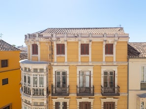 A multi-story building with a yellow facade, large windows with shutters, and a tiled roof. - Centrally located apartment with a terrace (Málaga)