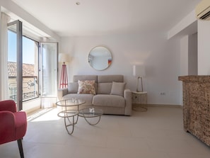 A living room with a sofa, two glass tables, a red floor lamp, a round mirror, and a patterned side table. - Centrally located apartment with a terrace (Málaga)