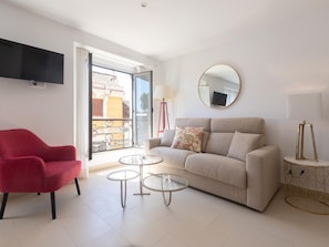 A modern living room with a sofa, a red chair, two glass tables, a TV, and a balcony with a view. - Centrally located apartment with a terrace (Málaga)