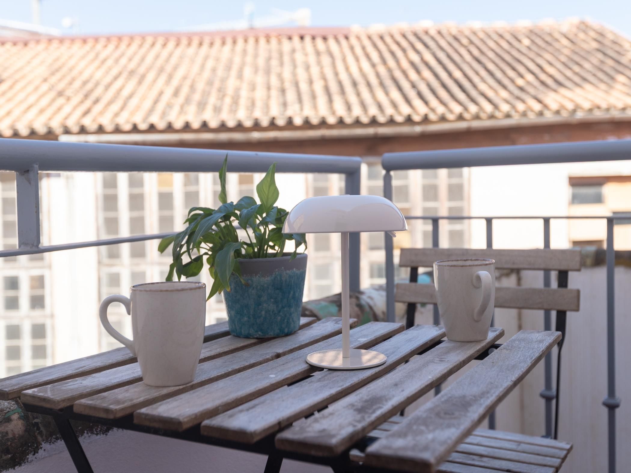 Un balcón con una mesa de madera, una planta en maceta y dos tazas blancas.