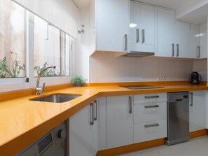 A modern kitchen with white cabinets, a wooden countertop, a built-in dishwasher, and a window with a view of plants. - Centrally located apartment with a terrace (Málaga)