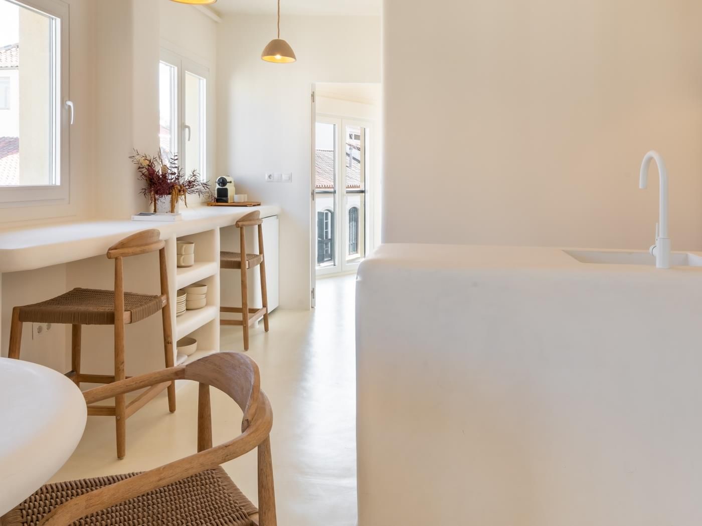 A modern kitchen with a white countertop, wooden chairs, a white sink, and a pendant light.