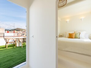 A hotel room with a bed, a small table, and a chair. There is a view of a cityscape through a window. - Penthouse with exclusive terrace, pool, and panoramic views (Málaga)