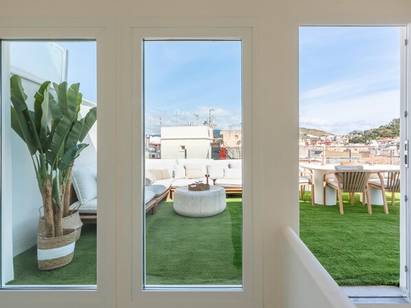 A view through a window of a rooftop with a green lawn, outdoor furniture, and a potted plant. - Penthouse with exclusive terrace, pool, and panoramic views (Málaga)