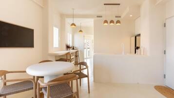 A modern kitchen with white cabinetry, a dining area with a white table and wooden chairs, and pendant lighting.