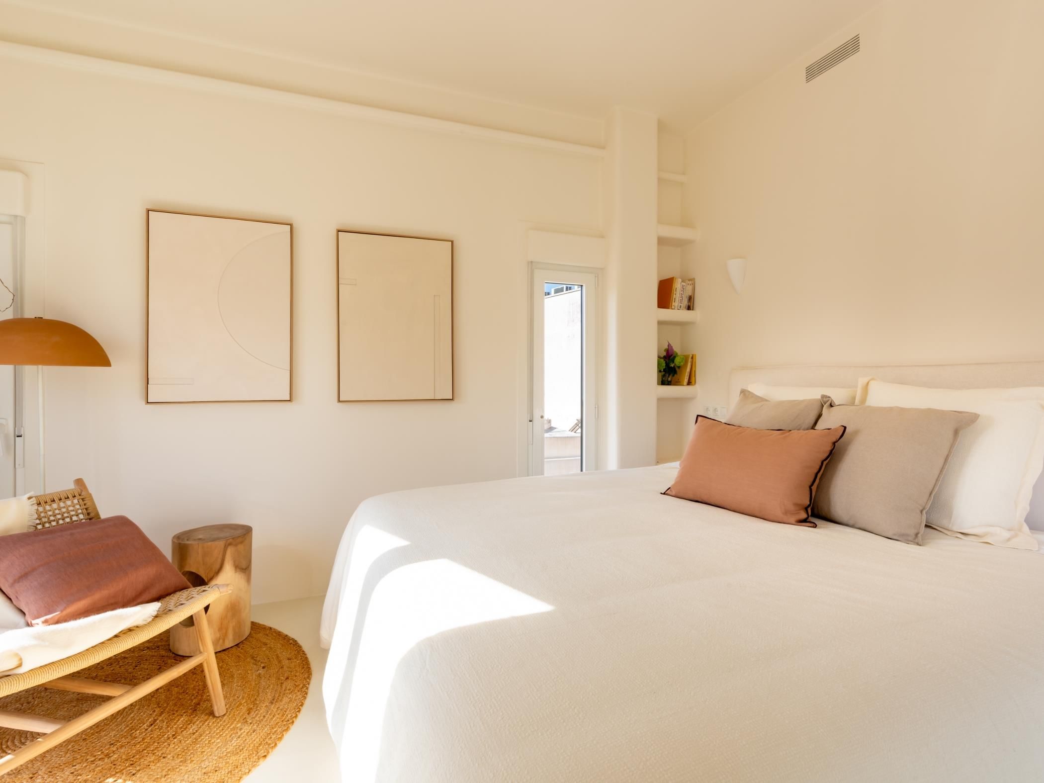 A bedroom with a large bed, a chair, a lamp, and two framed pictures on the wall.