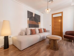 A modern living room with a sofa, a round wooden coffee table, a lamp, and a door. - Elegant and bright three-bedroom, two-bathroom apartment (Málaga)
