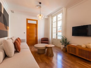 A modern living room with a sofa, a round coffee table, a red chair, a TV, and a potted plant. - Elegant and bright three-bedroom, two-bathroom apartment (Málaga)