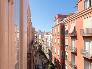 A narrow urban street with multi-story buildings, balconies, and a clear sky. - Elegant and bright three-bedroom, two-bathroom apartment (Málaga)