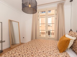 A bedroom with a bed, a hanging light fixture, a mirror, and a view of the outside. - Elegant and bright three-bedroom, two-bathroom apartment (Málaga)