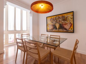 A dining area with a glass table and woven chairs, a painting on the wall, and a large window with curtains. - Elegant and bright three-bedroom, two-bathroom apartment (Málaga)