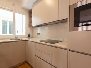 A modern kitchen with a built-in oven, a window with blinds, and a stainless steel refrigerator. - Elegant and bright three-bedroom, two-bathroom apartment (Málaga)