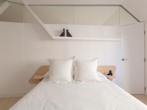A minimalist bedroom with a bed, two pillows, a wooden nightstand, and a white wall. - Balcones de San Juan (Málaga)