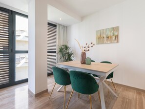 Ein moderner Essbereich mit einem Holztisch, grünen Samtstühlen, einer Vase mit getrockneten Pflanzen und einem Gemälde an der Wand.