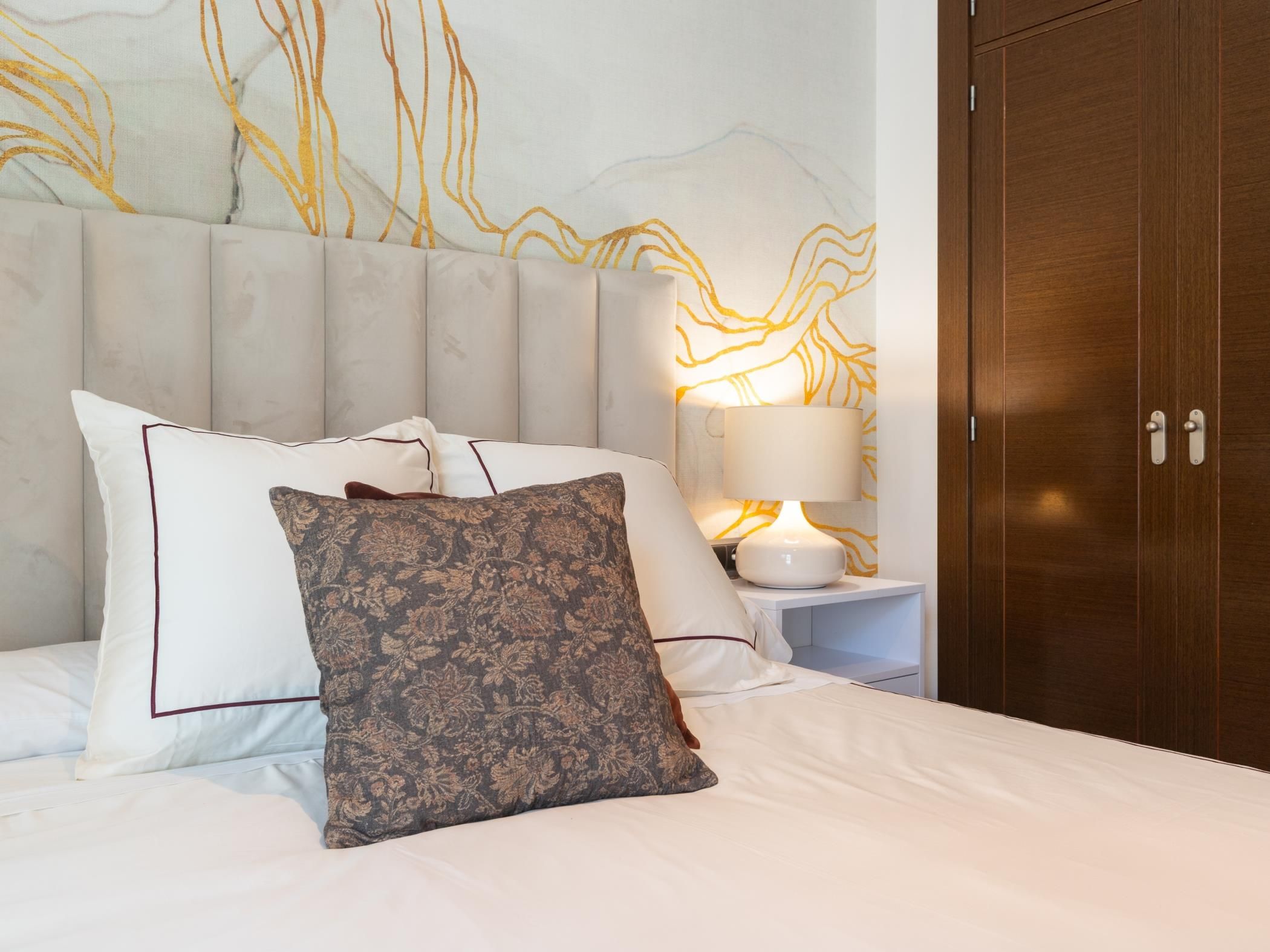 Un lit bien fait, agrémenté de plusieurs oreillers, une lampe de chevet et une armoire en bois dans une chambre d’hôtel.