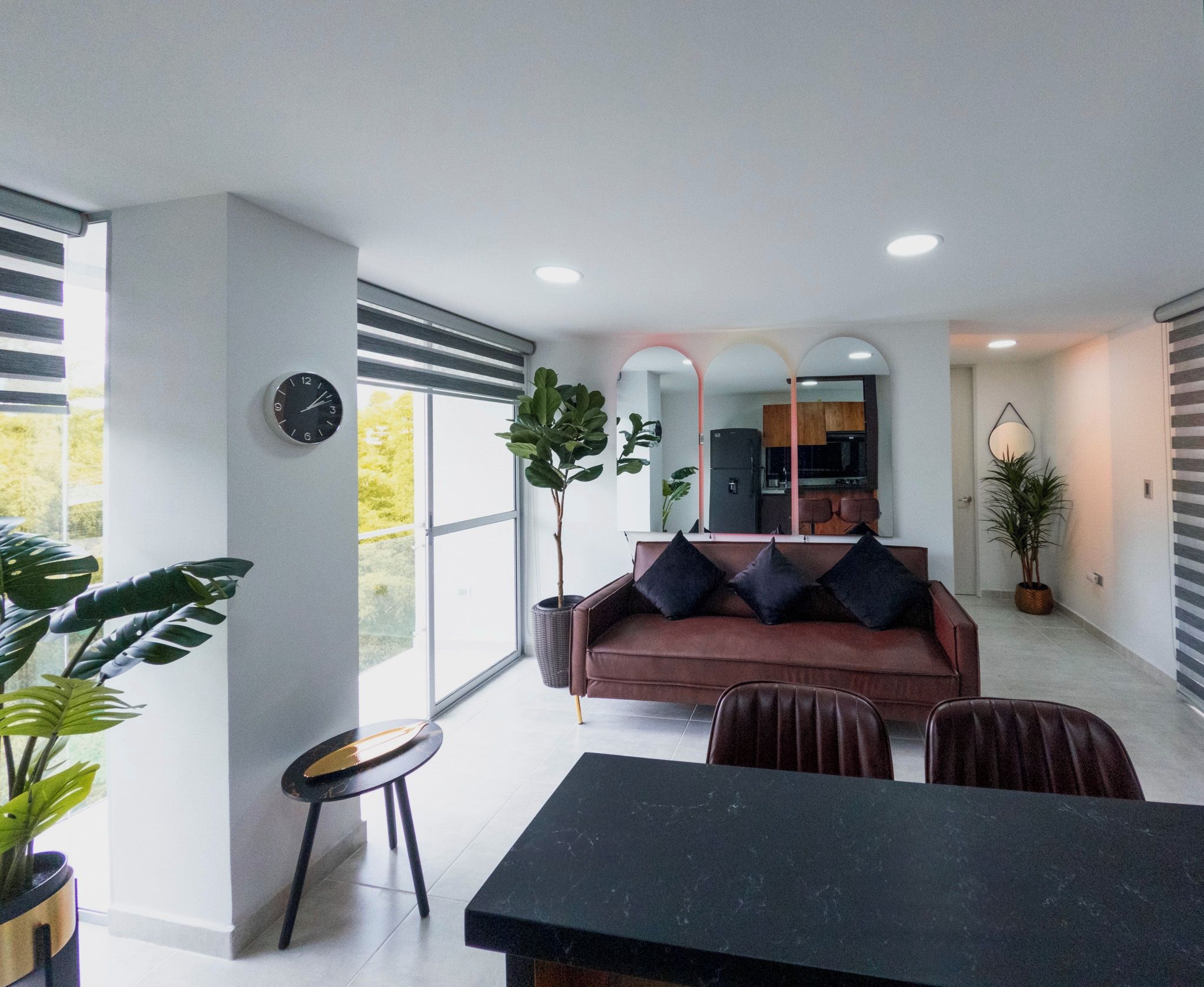 A modern living room with a sofa, chairs, a dining table, and a kitchen in the background.